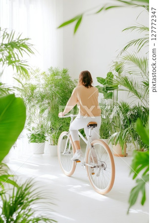 Indoor cycling scene with a person on a minimalist white bike surrounded by lush greenery, symbolizing fitness and sustainability 127772347