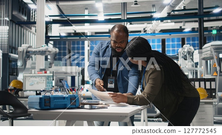 Black engineering professionals and directors review operational workflows in a solar manufacturing facility. Integrating teamwork in renewable energy production and development. Camera A. Black engineering professionals and directors review operational workflows in a solar manufacturing facility. Integrating teamwork in renewable energy production and development. Camera A. 127772545