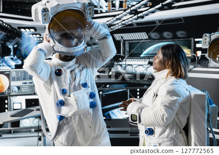 Researcher travelling in space with starship putting helmet on, talking with colleague, conducting scientific experiments. Scientist dressing in equipment, chatting with coworker during cosmic journey Researcher travelling in space with starship putting helmet on, talking with colleague, conducting scientific experiments. Scientist dressing in equipment, chatting with coworker during cosmic journey 127772565