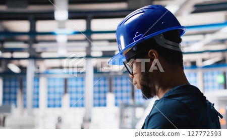 Black photovoltaics factory technician looking over paperwork documents, analyzing data for production. Solar panels manufacturing plant worker reading files to troubleshoot errors. Camera A. 127772593
