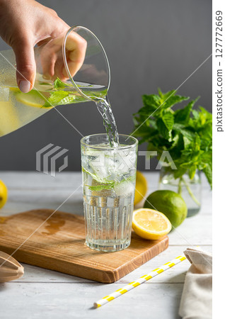 Lemonade with lemons, limes and fresh mint. Pouring homemade lemonade in a glass 127772669
