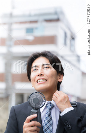 A busy businessman working in the heat - Cooling off with a handheld fan 127773089