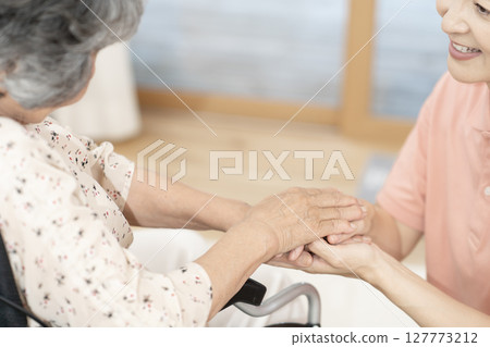 女性照護人員與坐輪椅的老年婦女交談身體部位握手握手溝通 127773212