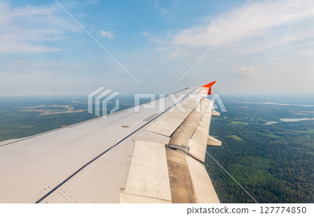 View of airplane wing, blue skies and green land during landing. Airplane window view. View of airplane wing, blue skies and green land during landing. Airplane window view. 127774850