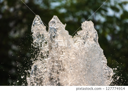 Splashes of water on dark background. Water sprays in sunny day close-up. Splashes of water on dark background. Water sprays in sunny day close-up. 127774914