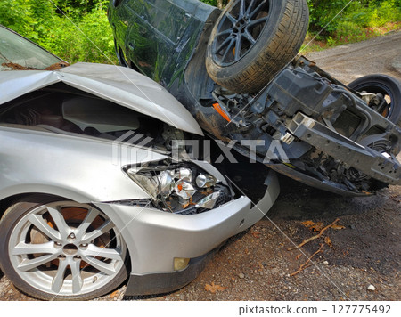 Serious car accident on quiet road involves damaged silver sedan an overturned black car. 127775492