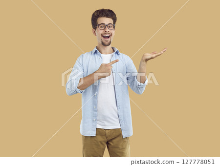 Laughing happy bearded man pointing index fingerand hand on copy space on beige background. 127778051