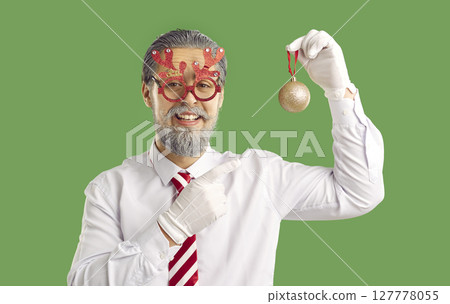Handsome man dressed in festive clothing, being Santa Claus, pointing at Christmas tree decoration 127778055