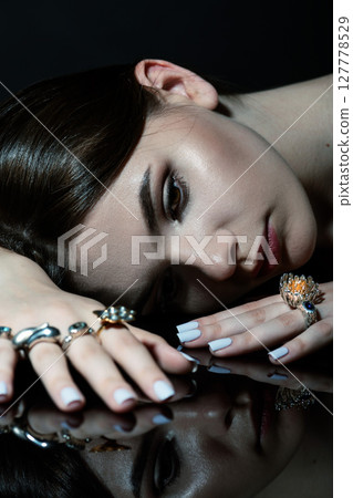 Studio portrait of beautiful and sexy brunette woman with fancy make-up and various rings on her fingers 127778529