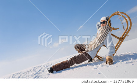Child is resting on a sleigh in the snow. 127781969