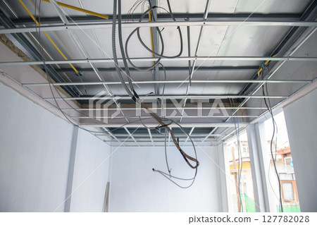Messy but organized interior renovation project showing electrical wiring installation within an aluminium ceiling framework. room captures feeling of progress and change 127782028
