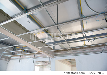 Raw interior renovation showing aluminium ceiling framework. complex electrical wiring installation is visible during construction phase of building project 127782032