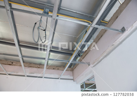 Detailed view of an interior renovation showing electrical wiring installation within new aluminium ceiling framework part of home improvement project Detailed view of an interior renovation showing electrical wiring installation within new aluminium ceiling framework part of home improvement project 127782038