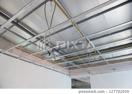 Aluminium ceiling framework with new electrical wiring shows installation progress during an interior renovation project. metal grid structure supports unfinished ceiling Aluminium ceiling framework with new electrical wiring shows installation progress during an interior renovation project. metal grid structure supports unfinished ceiling 127782039