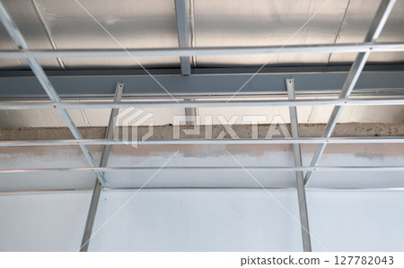Hopeful progress of interior renovation with aluminium ceiling framework. electrical wiring installation reveals complex grid system during home improvement project 127782043