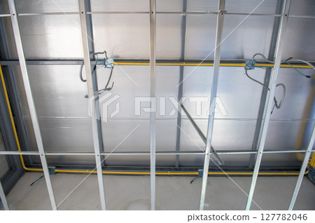 Focused view of ceiling construction during an interior renovation. metal framework supports aluminium insulation with complex electrical wiring installation in progress 127782046