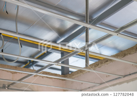 Interior renovation project focuses on ceiling framework installation. Exposed electrical wiring runs along new aluminium grid system before final finishing 127782048