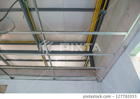 Diligent interior renovation showing electrical wiring installation within an aluminium ceiling framework. process details structural progress of modern building project Diligent interior renovation showing electrical wiring installation within an aluminium ceiling framework. process details structural progress of modern building project 127782053