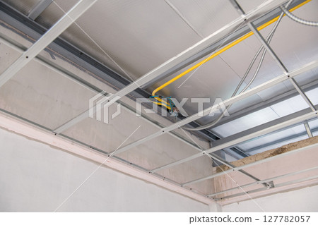 Focused view on an interior renovation project showing complex electrical wiring and conduit during installation above new suspended aluminium ceiling framework and grid system Focused view on an interior renovation project showing complex electrical wiring and conduit during installation above new suspended aluminium ceiling framework and grid system 127782057