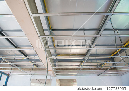 Interior renovation project showing new ceiling installation. An aluminium framework with complex electrical wiring hangs below unfinished slab showing sense of progress 127782065