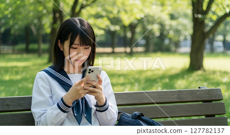 A high school girl operating a smartphone on a park bench 127782137