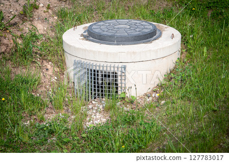 Underground Concrete Utility Access with Manhole Cover and Grated Drain Vent in Grass Field 127783017
