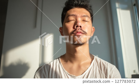 Calm Young Man Meditating in Sunlight with Closed Eyes 127783072