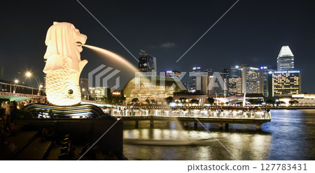 Night view of the Merlion with the background of modern skyscrapers in Marina Bay, Singapore. The Merlion is the official mascot of Singapore. 127783431