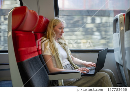 Woman working on laptop while traveling by train in daylight, concept of remote work and travel 127783666