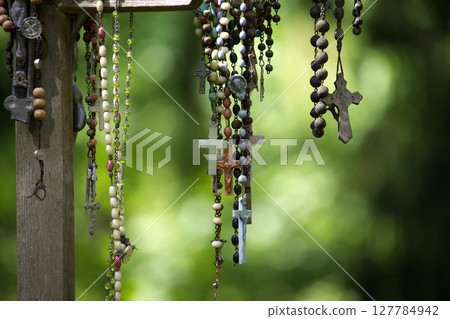 Various rosaries with crosses and beads hang against a soft, green backdrop. Various rosaries with crosses and beads hang against a soft, green backdrop. 127784942
