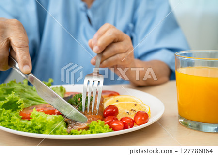 Asian elderly woman patient eating salmon stake and vegetable salad for healthy food in hospital. 127786064