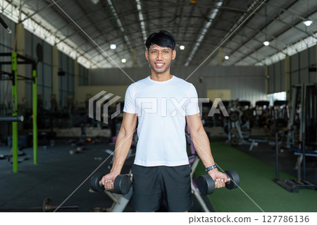 Fitness and Strength Training. Young man lifting dumbbells in gym for strength and wellness. 127786136