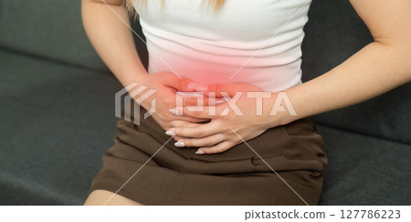 Abdominal Discomfort. Young woman holding her stomach in pain while sitting. 127786223