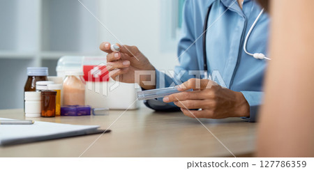Doctor Preparing Medication. Healthcare professional holding a vial and syringe in a clinical environment. 127786359