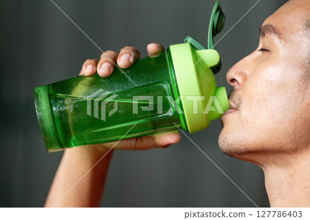 Hydration and Fitness. Man drinking from a green shaker bottle, emphasizing health and wellness. 127786403