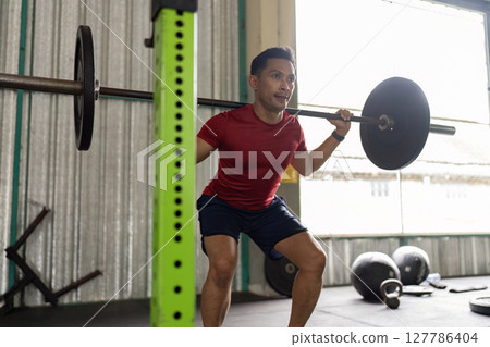 Strength Training. Young man performing squats with barbell in gym. Strength Training. Young man performing squats with barbell in gym. 127786404