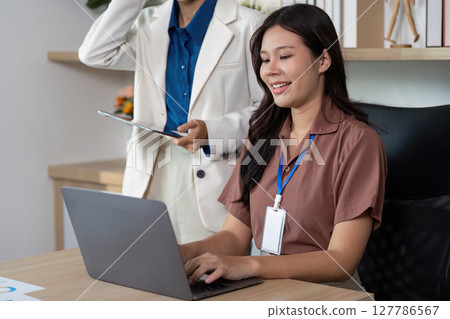 Productivity in the Office. Woman smiling while working on a laptop with a supportive colleague. 127786567