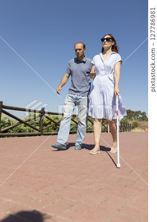Man helping blind woman walking with white cane in park on sunny day 127786981