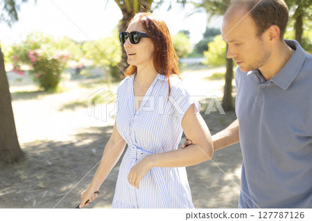Nurse assisting blind woman walking in park with white cane 127787126