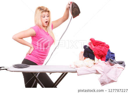 Shocked woman holding iron about to do ironing 127787227