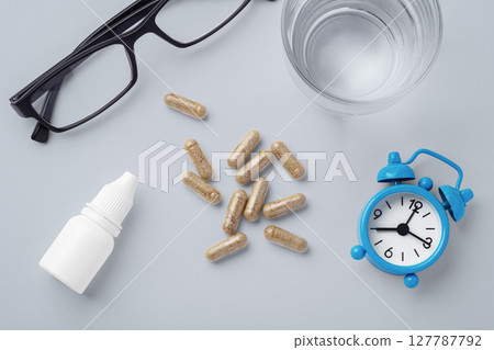 Supplement, vitamin capsule with eye glasses, eye drops and clock on table, supplement for eye health and vision 127787792