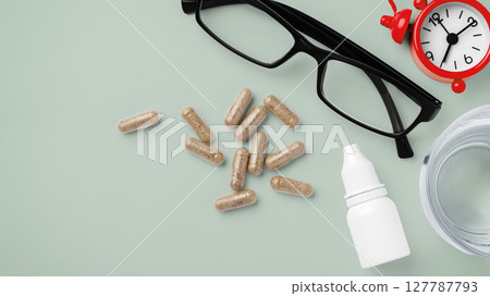 Natural supplement, vitamin capsule with eye glasses, eye drops and clock on green background, supplement for eye health and vision, top view Natural supplement, vitamin capsule with eye glasses, eye drops and clock on green background, supplement for eye health and vision, top view 127787793