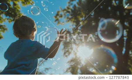 Low-angle shot of a child joyfully playing with bubbles in a park, with sunlight gleaming through the trees. 127787843