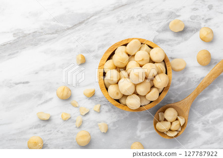 Macadamia nuts in wooden bowl with spoon and cracked macadamia on marble kitchen countertop background, top view Macadamia nuts in wooden bowl with spoon and cracked macadamia on marble kitchen countertop background, top view 127787922
