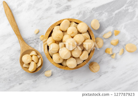 Macadamia nuts in wood bowl with spoon and cracked macadamia on marble table background, top view Macadamia nuts in wood bowl with spoon and cracked macadamia on marble table background, top view 127787923