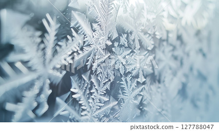 Macro shot captures intricate ice crystals on a windowpane, showcasing delicate patterns in stunning detail. 127788047