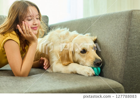 Teen girl enjoys playtime with her golden retriever in a cozy living room setting 127788083