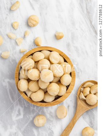 Macadamia nuts in wooden bowl with spoon and cracked macadamia on marble table background 127788612