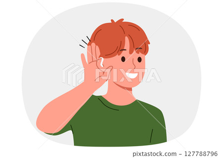 Boy uses hearing aid and puts palm to ear, smiles listening to sounds around him. 127788796