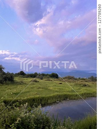Summer evening landscape. Beautiful sky, colorful clouds, green grass and blue river 127789260